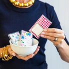 Person holding a bowl with playing cards and a deck of cards on a plain background