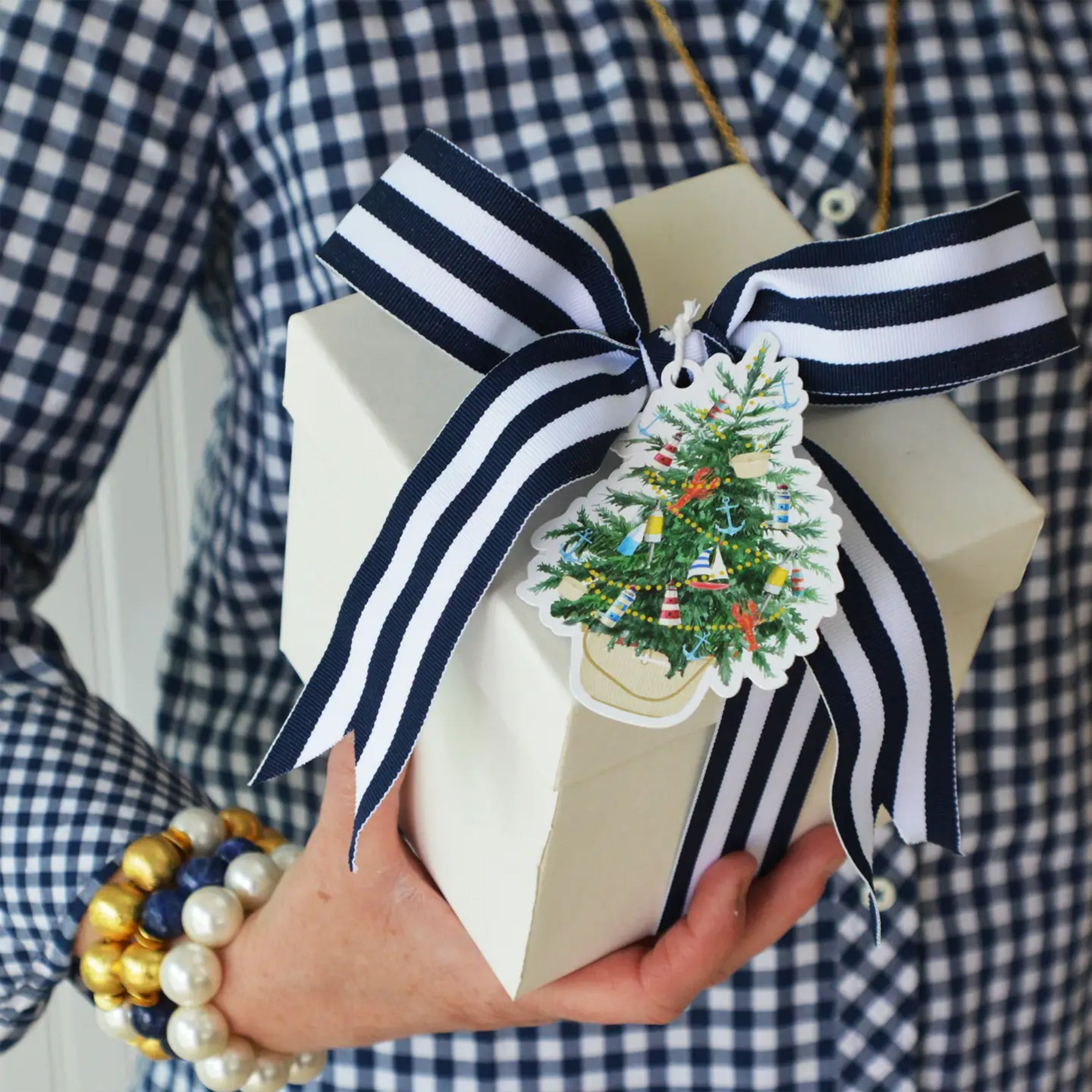 Gift box with a striped ribbon and Christmas tree ornament held by a person wearing a checkered shirt.