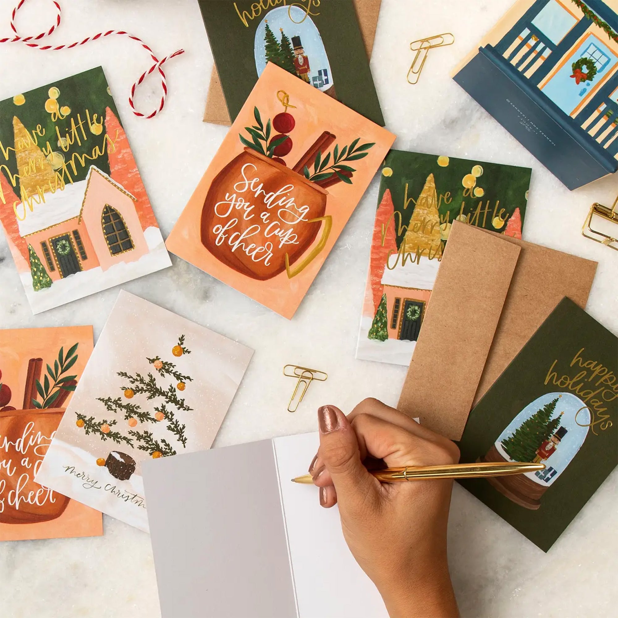 Collection of Christmas-themed greeting cards and envelopes on a white surface with a hand writing.