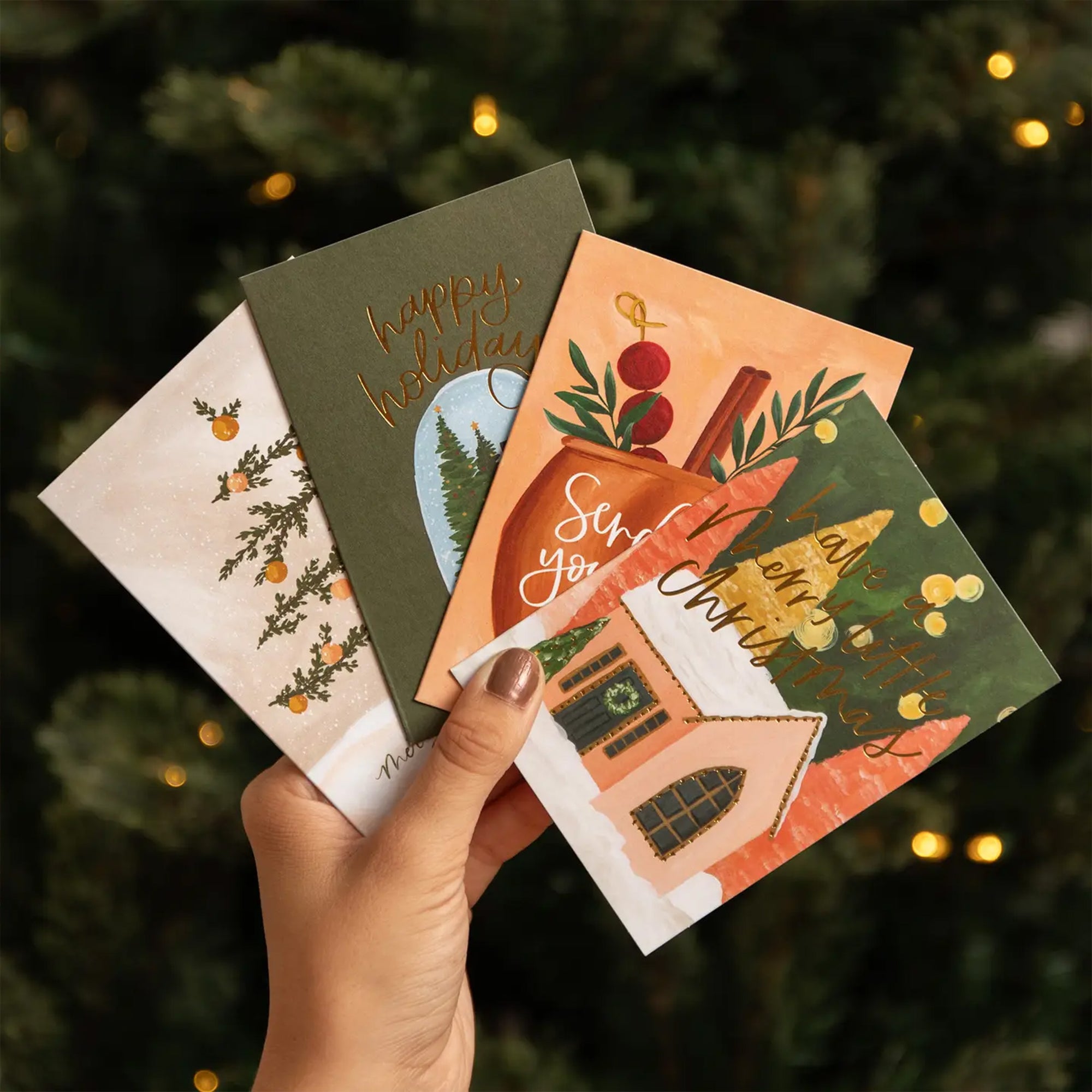 Hand holding four Christmas-themed cards with a festive background