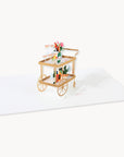 Decorative card with a gold cart holding flowers and bottles on a white background