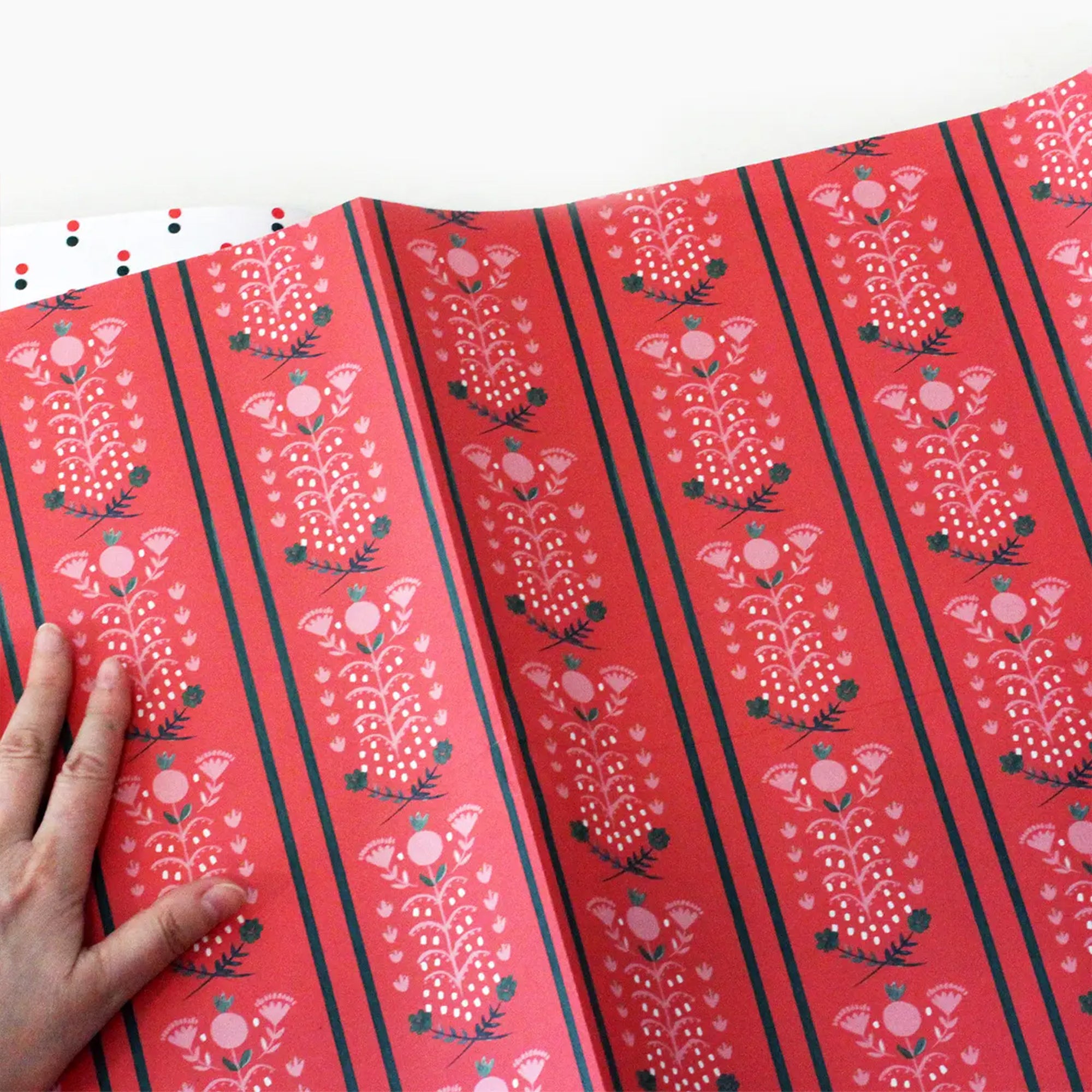 Red wrapping paper with floral patterns and black stripes, held by a hand.