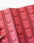 Red wrapping paper with floral patterns and black stripes, held by a hand.
