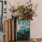 Book titled 'The Odyssey' by Homer with a decorative vase containing dried flowers on a wooden surface.
