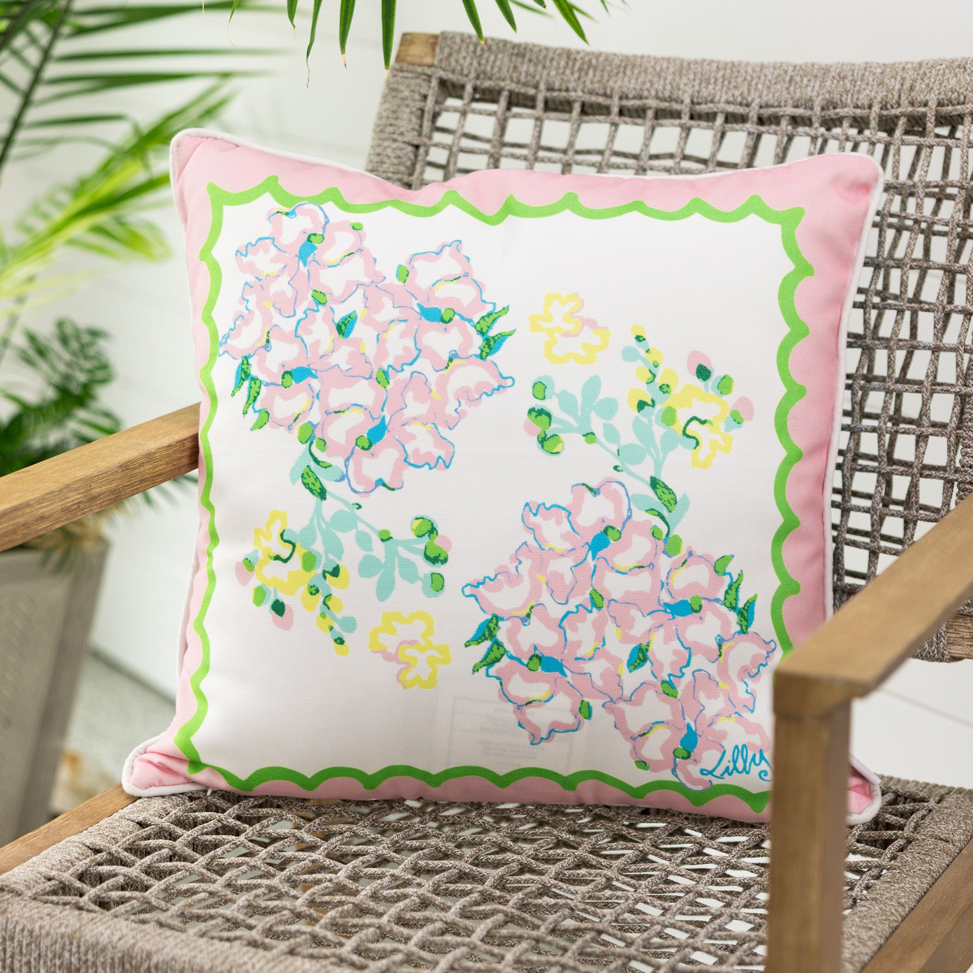 Floral pillow with pink and green border on a wicker chair