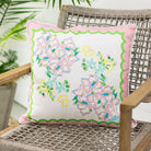 Floral pillow with pink and green border on a wicker chair