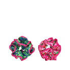 Two fabric hair scrunchies on a plain white background. One scrunchie has a green tropical leaf pattern with bright pink trim, and the other has a pink floral print with red trim.