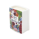 A square white candle vessel with a ribbed side and a colorful illustrated front panel featuring flowers and the text 'Alice's Adventures Wonderland'