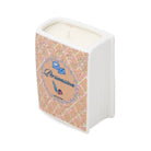 A novelty candle shaped like a book, featuring a white ribbed spine and cover with a pink floral lattice pattern, a central blue circular label reading 'Persuasion', and cream-colored wax visible at the top.