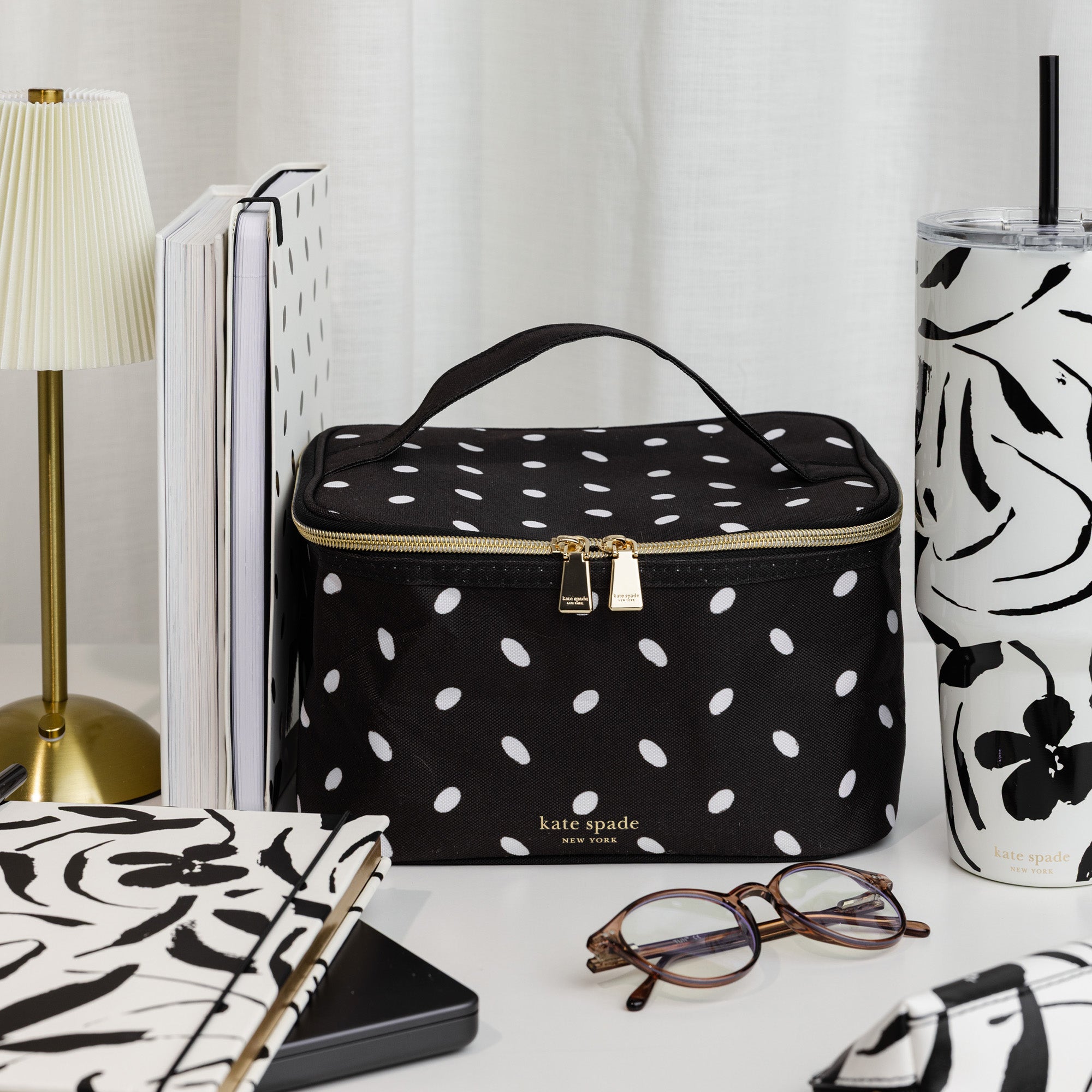 Black polka dot lunch bag with 'kate spade' branding on a white surface with decorative items.
