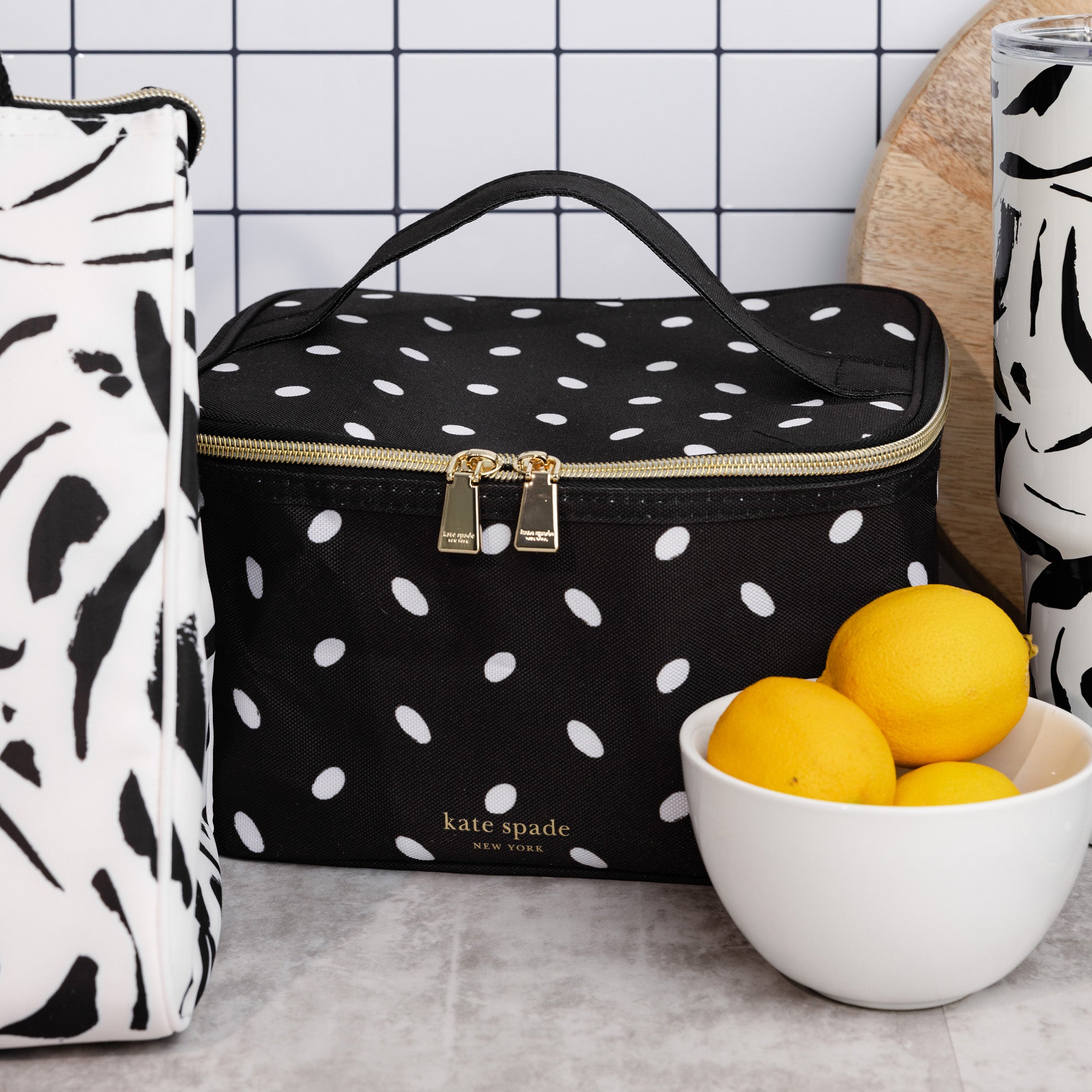 Black polka dot cooler bag with gold zipper on a kitchen counter, next to a bowl of lemons.