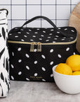 Black polka dot cooler bag with gold zipper on a kitchen counter, next to a bowl of lemons.