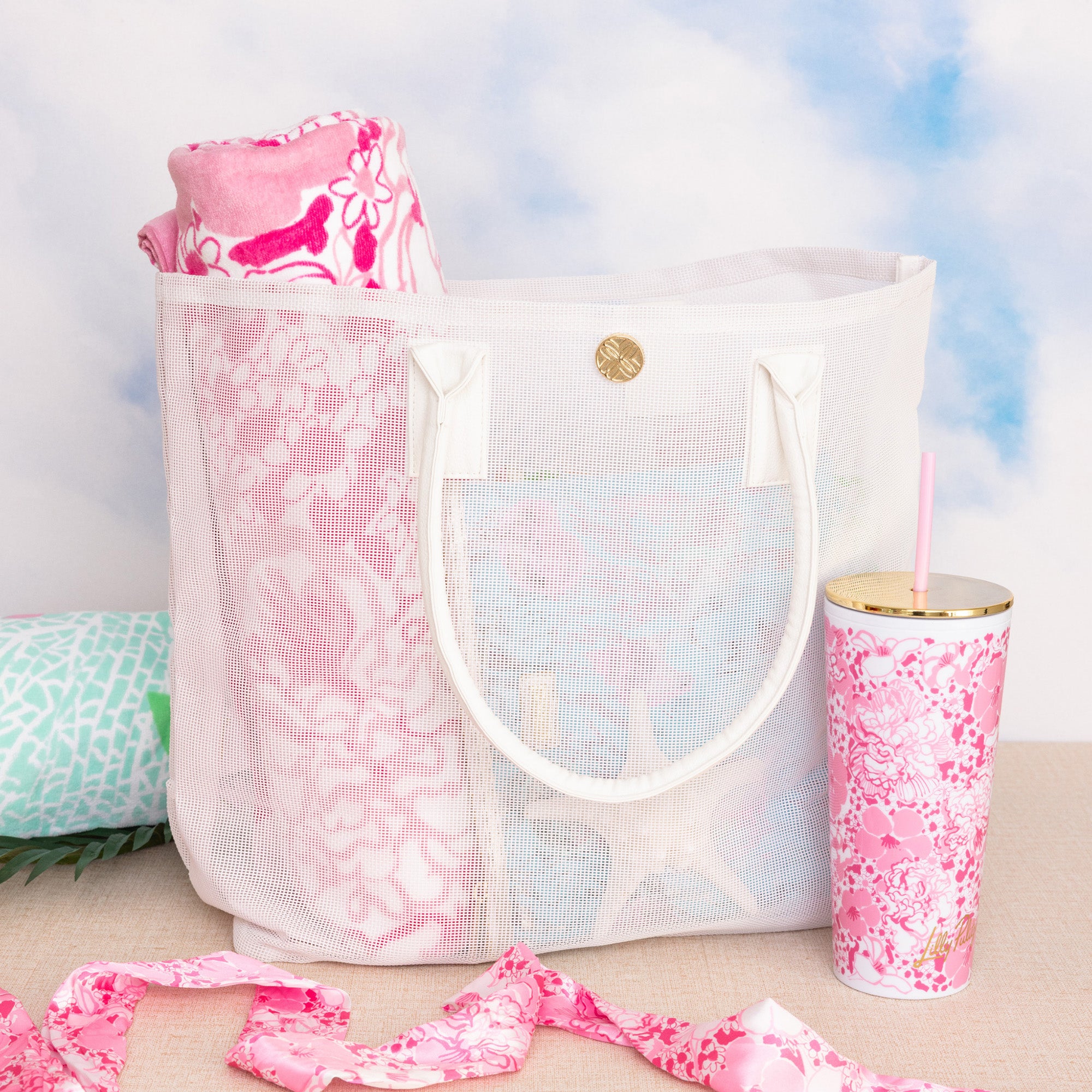 white mesh beach bag with a pink floral towel and matching tumbler