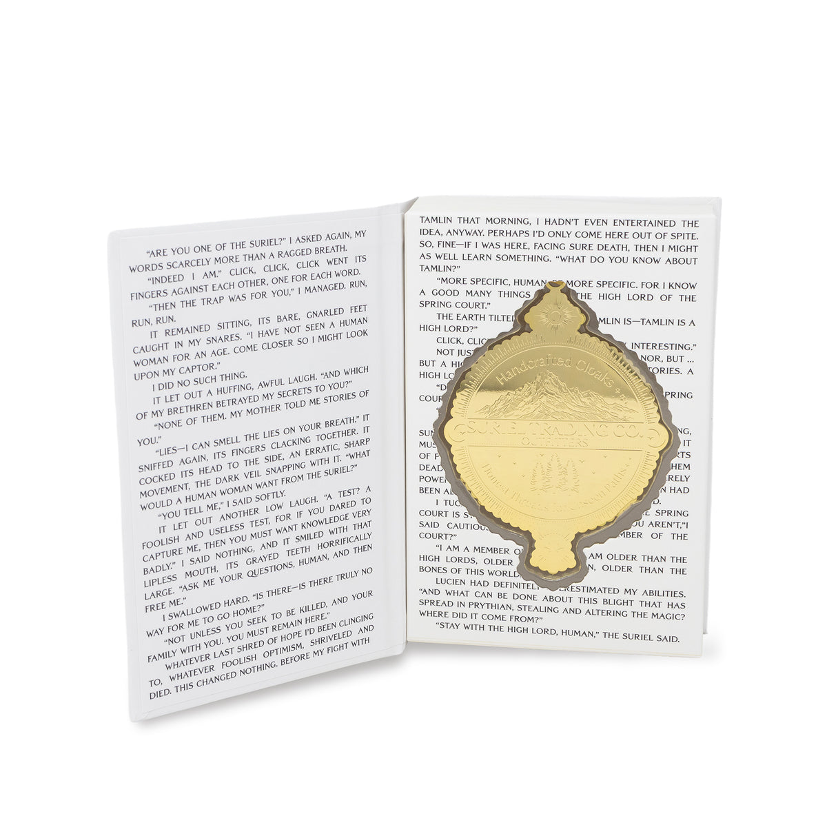 suriel trading co. embossed gold ornament with gold hanging ribbon, displayed on in an open book with printed text.
