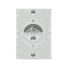 A rectangular book packaging with a white background and an intricate sage green floral and mountain pattern. The center features a circular logo for 'Suriel Trading Co.