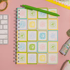 Notebook with sun tile on a pink surface with stationery items.
