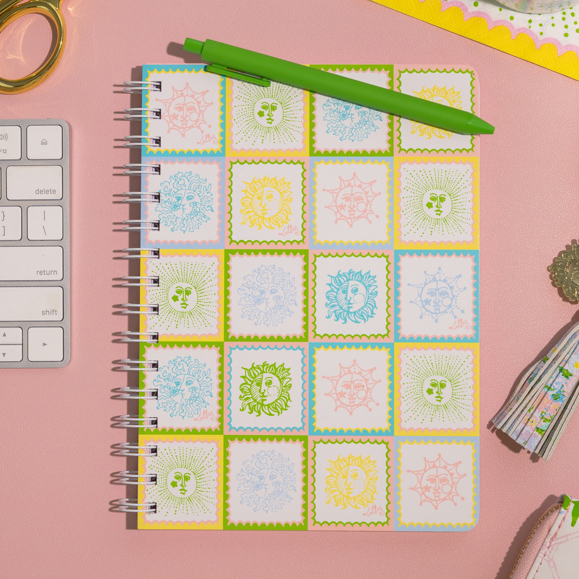 Notebook with sun tile on a pink surface with stationery items.