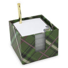A square green plaid notepad holder box with a gold pen inserted into the top, holding white notepads. The box features a green tartan pattern with black and pinkish stripes, and a small decorative emblem is visible on the notepad.