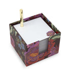 A square notecube with a colorful floral pattern and containing a gold metal pen on white tissue paper.