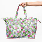 model holding a large tote bag with a colorful patchwork print featuring cartoon characters and text in pink, green, blue, and white