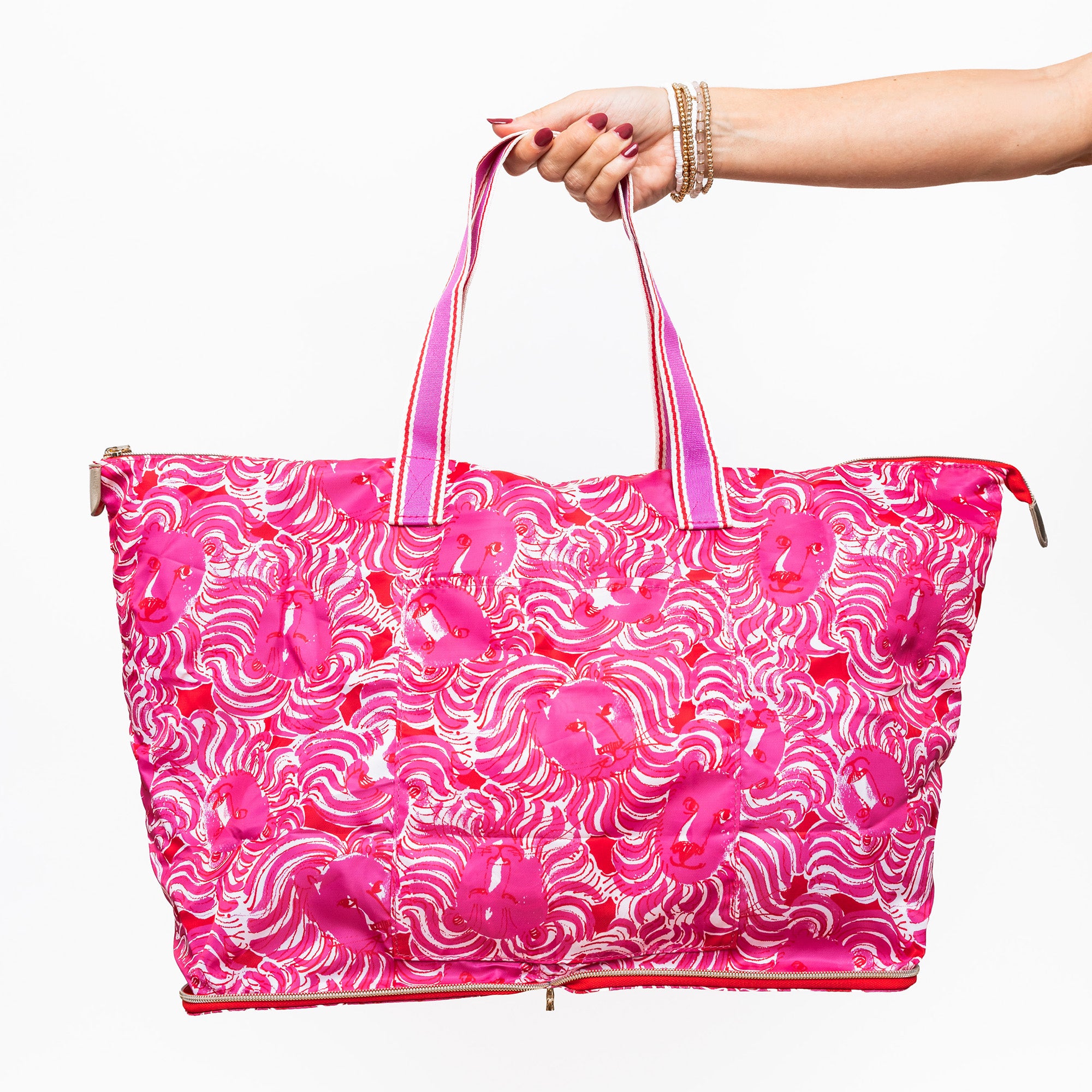 model holding a bright pink tote bag with a white wavy floral pattern, featuring dual pink-and-white striped shoulder straps and a zippered closure
