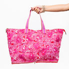 model holding a bright pink tote bag with a white wavy floral pattern, featuring dual pink-and-white striped shoulder straps and a zippered closure