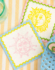 Two decorative napkins with sun designs on a striped surface.