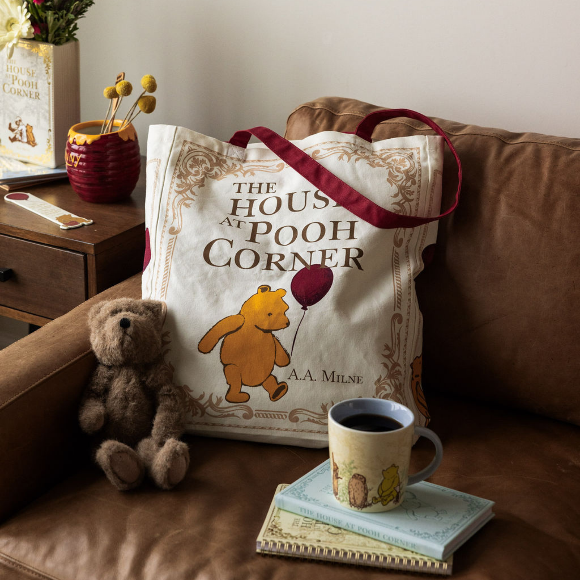 Tote bag with Winnie the Pooh design on a couch next to a teddy bear and a cup of coffee.