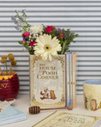 Decorative setup with 'The House at Pooh Corner' book, flowers, and Winnie the Pooh-themed items against a striped background.