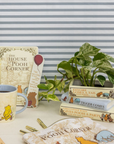 Winnie the Pooh-themed items including a mug, books, and a plant on a striped background