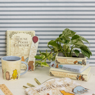 Winnie the Pooh-themed items including a mug, books, and a plant on a striped background