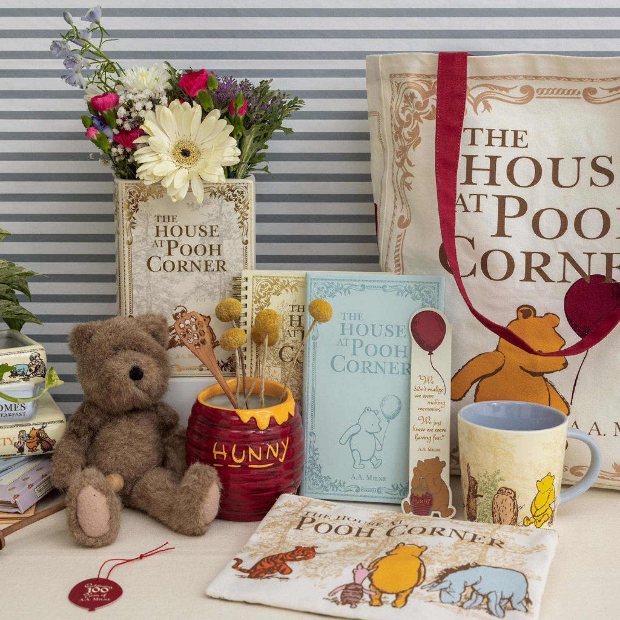 Collection of Winnie the Pooh-themed items including a teddy bear, mug, and books on a striped background.