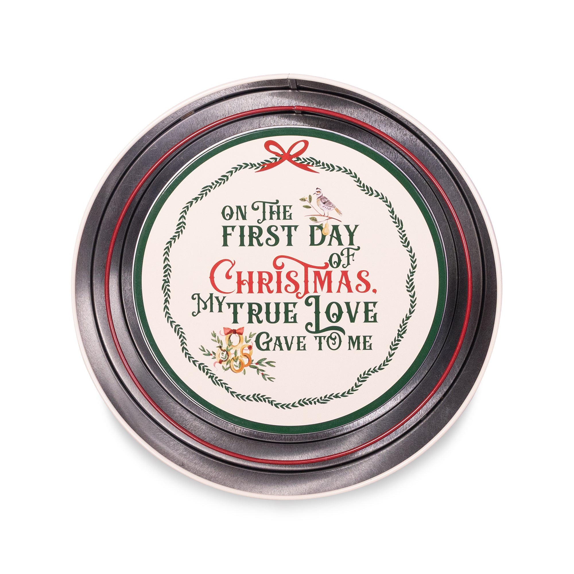A round tin with a silver metal lid featuring a festive Christmas design. The lid has a cream-colored center with the text 'ON THE FIRST DAY OF CHRISTMAS, MY TRUE LOVE I GAVE TO ME' in green and red lettering, surrounded by a wreath border, a small bird, and a red bow.
