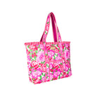 A bright pink tote bag with a floral print, featuring pink and white striped handles and a small gold brand plaque on the front.