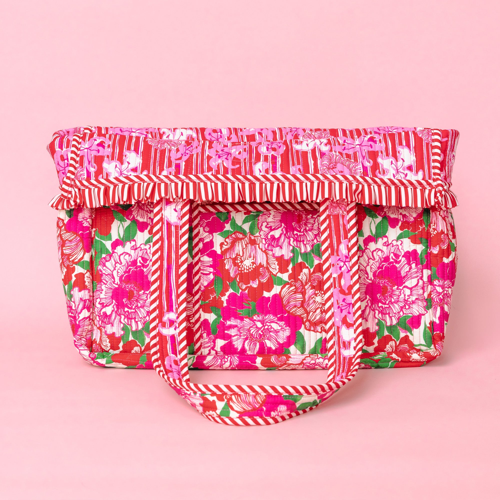 folded down bright pink tote bag with a floral print, featuring pink and white chevron-patterned handles and a small  brand patch on the front.