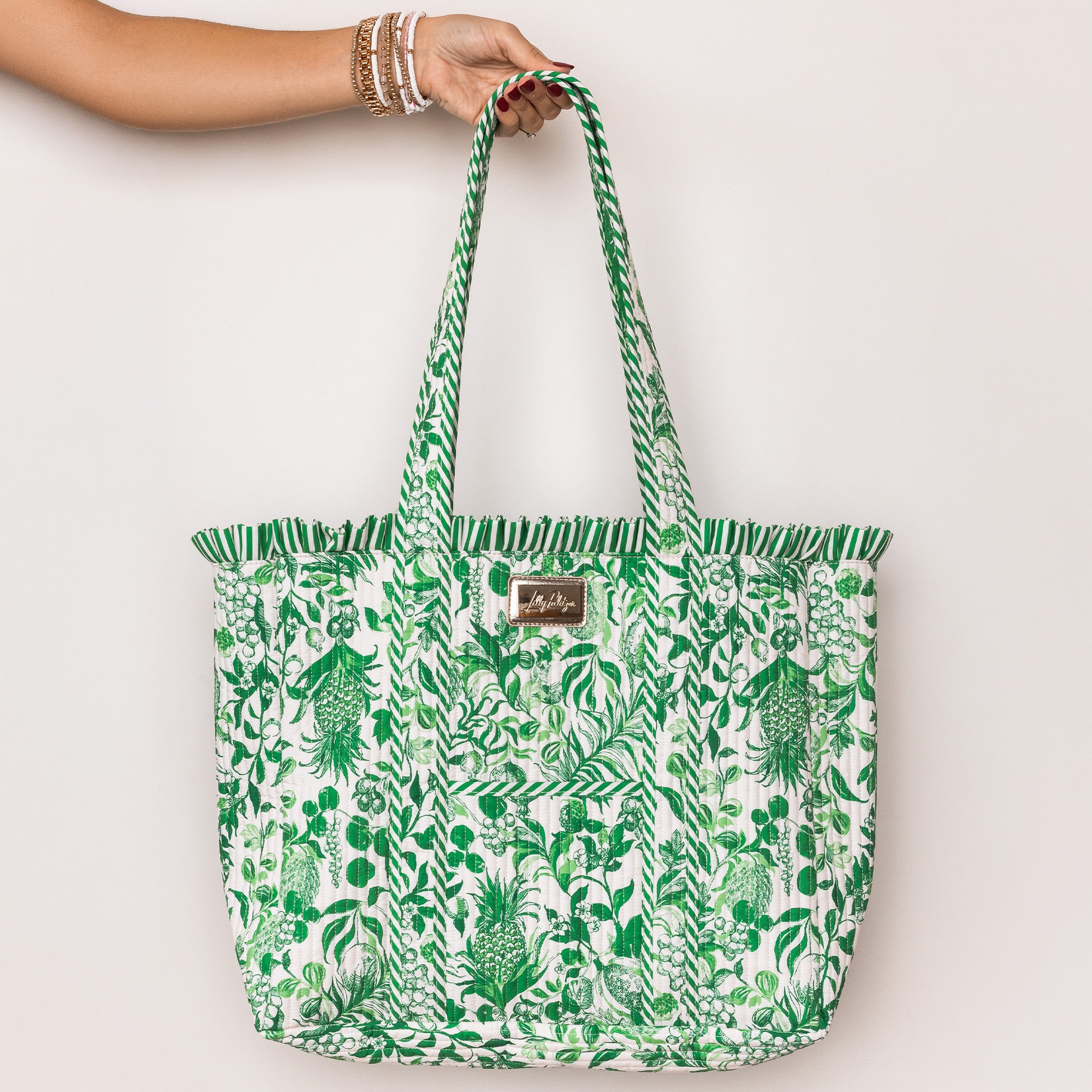 model holding a green and white tropical botanical print tote bag with ruffled trim and long shoulder straps