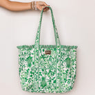 model holding a green and white tropical botanical print tote bag with ruffled trim and long shoulder straps