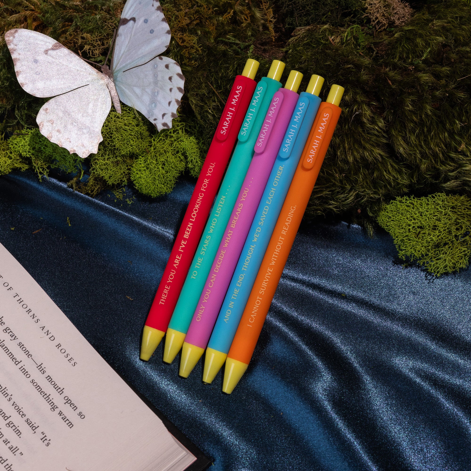 Five colorful pens with yellow tips on moss and a silky navy backdrop