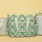 A green and pink patterned tote bag with scalloped edges and light green handles, shown alongside matching patterned bags on a pale yellow background.