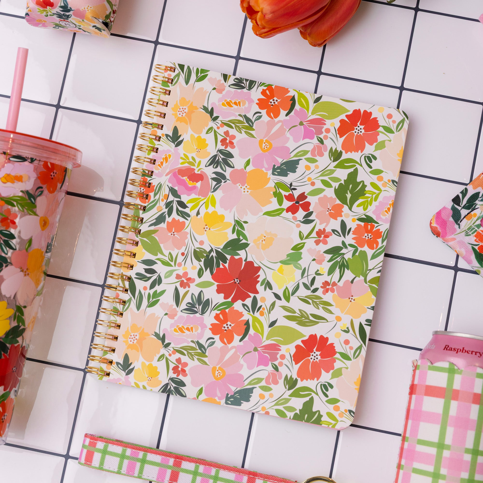 Floral notebook on a tiled surface with a pink tumbler and other stationery items.