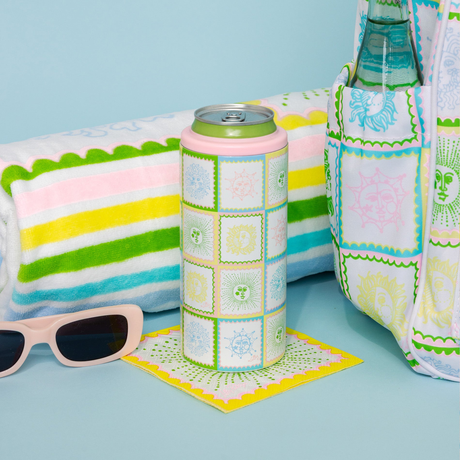 Colorful can cooler, bottle holder, and sunglasses on a blue surface with a towel in the background.