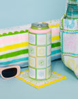 Colorful can cooler, bottle holder, and sunglasses on a blue surface with a towel in the background.