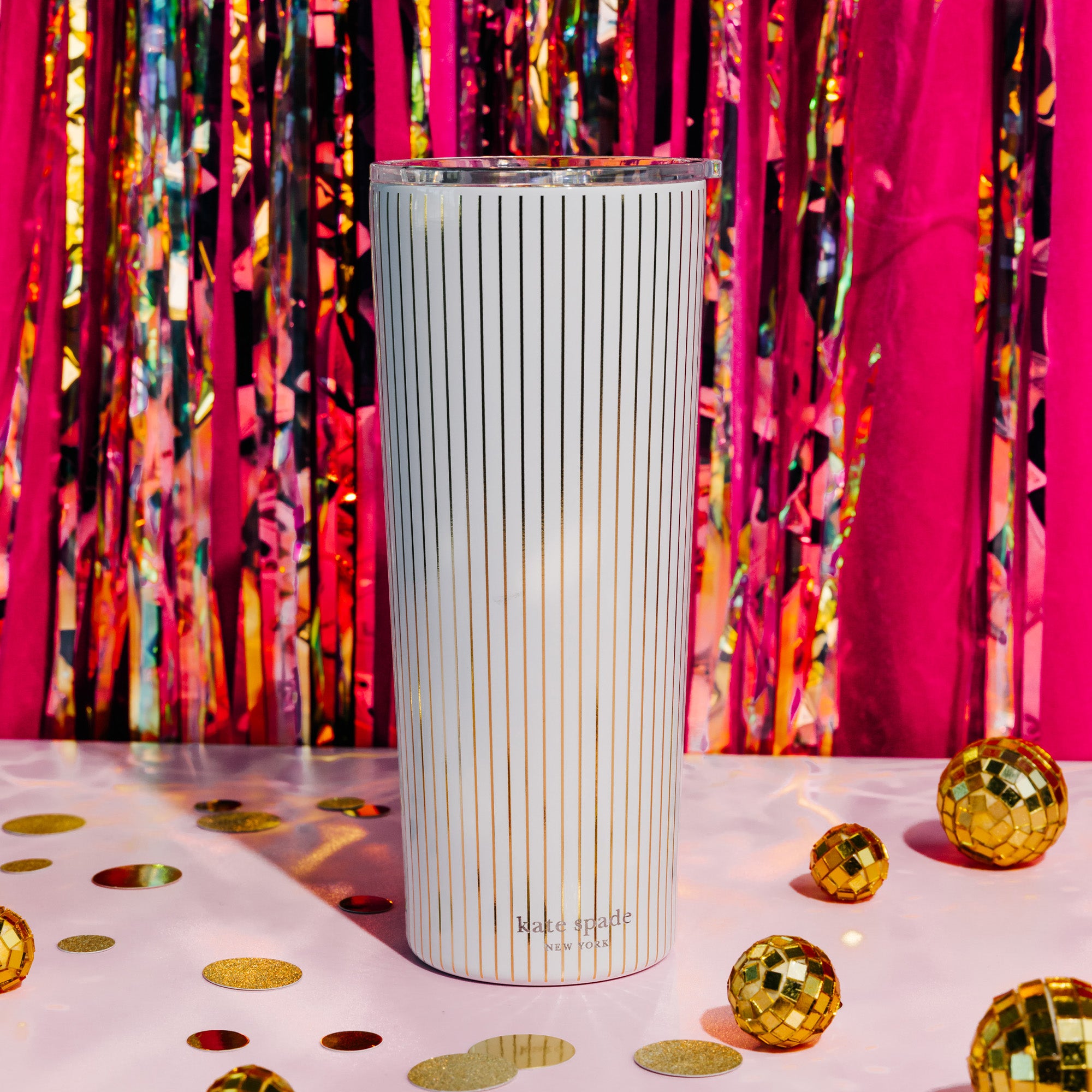 A tall insulated tumbler with a clear lid, featuring a white body with thin vertical gold stripes