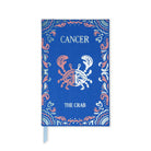 A blue hardcover journal or notebook featuring a zodiac design for Cancer 'The Crab'. The cover has a blue linen texture background with a coral pink and white crab illustration in the center, surrounded by a decorative paisley border.