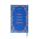 A blue hardcover journal by Kate Spade New York with a decorative paisley border in coral pink, light blue, and white, featuring the words 'DREAMY DEVOTED INTUITIVE EXPRESSIVE' in coral text. A light blue ribbon bookmark is visible on the right side, set against a plain white background.