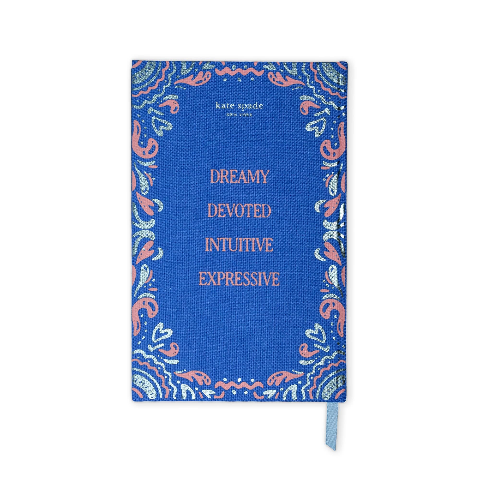 A blue hardcover journal by Kate Spade New York with a decorative paisley border in coral pink, light blue, and white, featuring the words 'DREAMY DEVOTED INTUITIVE EXPRESSIVE' in coral text. A light blue ribbon bookmark is visible on the right side, set against a plain white background.