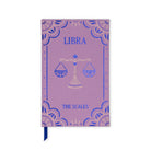 A lavender purple hardcover journal with a Libra zodiac theme, featuring a blue and gold scale of justice illustration and a blue ribbon bookmark.