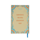 A hardcover journal by katt eyebits with a beige cover, decorated with a blue and orange mandala border and the words 'EMPATHETIC TRUSTING IMAGINATIVE DEEP' in orange. A blue ribbon bookmark is visible on the right side.