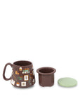 Brown ceramic mug with decorative elements, matching cup holder, and green lid on a white background