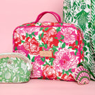 up close of rectangular cosmetic bag with a vibrant pink, red, and green floral print on a cream background, featuring pink handles and a gold-tone brand plaque.